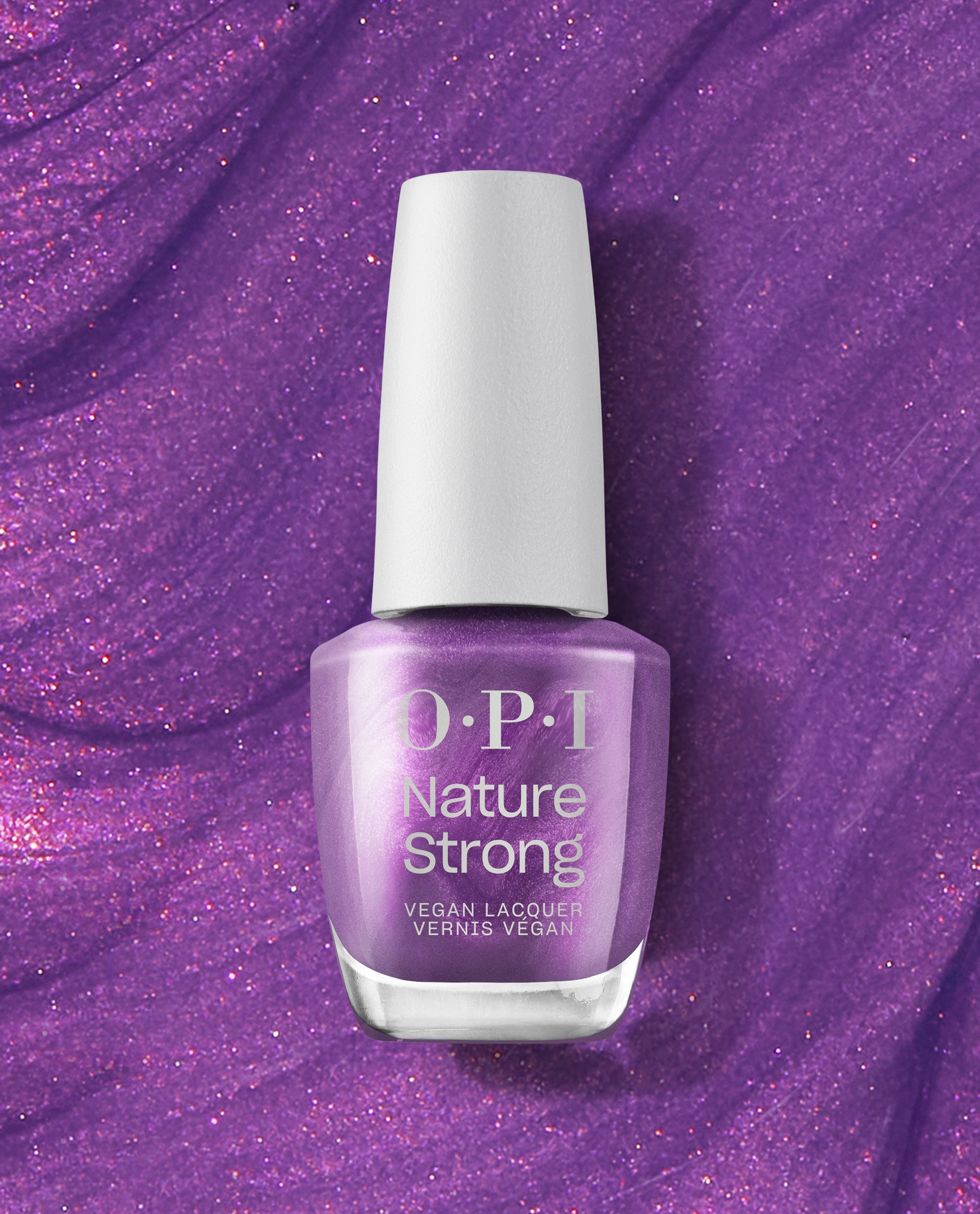 OPI Achieve Grapeness Nature Strong Vegan Nail Lacquer bottle stands upright, showing a shimmery grape-purple fall nail color against a sparkling purple textured background.