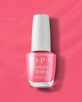 OPI Nature Strong Vegan Nail Lacquer in Big Bloom Energy, a trending bright pink-coral shade, stands upright with a white cap on a glossy pink background.