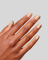 Hand displays glossy nude-beige OPI RapiDry nail polish in Can’t Hardly Wait, a trending neutral manicure shade, on short rounded nails against a light gray background.