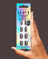 Hand holding OPI Sticking Point The Mani Espresso press-on nails in iridescent packaging, showing glossy dark espresso brown almond nails against a dark brown background.