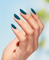 Almond-shaped nails painted a rich teal green, hand posed against a soft blue sky, showcasing OPI Nature Strong Vegan Nail Lacquer, All Heal Queen Mother Earth—a glossy green nail polish ideal for spring nail colors.