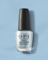 OPI Baggy Jean Baby nail lacquer stands upright, displaying a soft denim-blue creme polish on a matching blue studio backdrop, a chic addition to fall nail colors for US manicures.