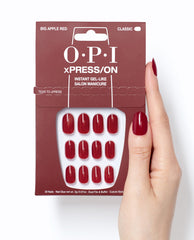 OPI Big Apple Red xPRESS/ON press-on nails in glossy classic red shown in retail packaging beside a hand wearing matching gel-like manicure nails on a white background.