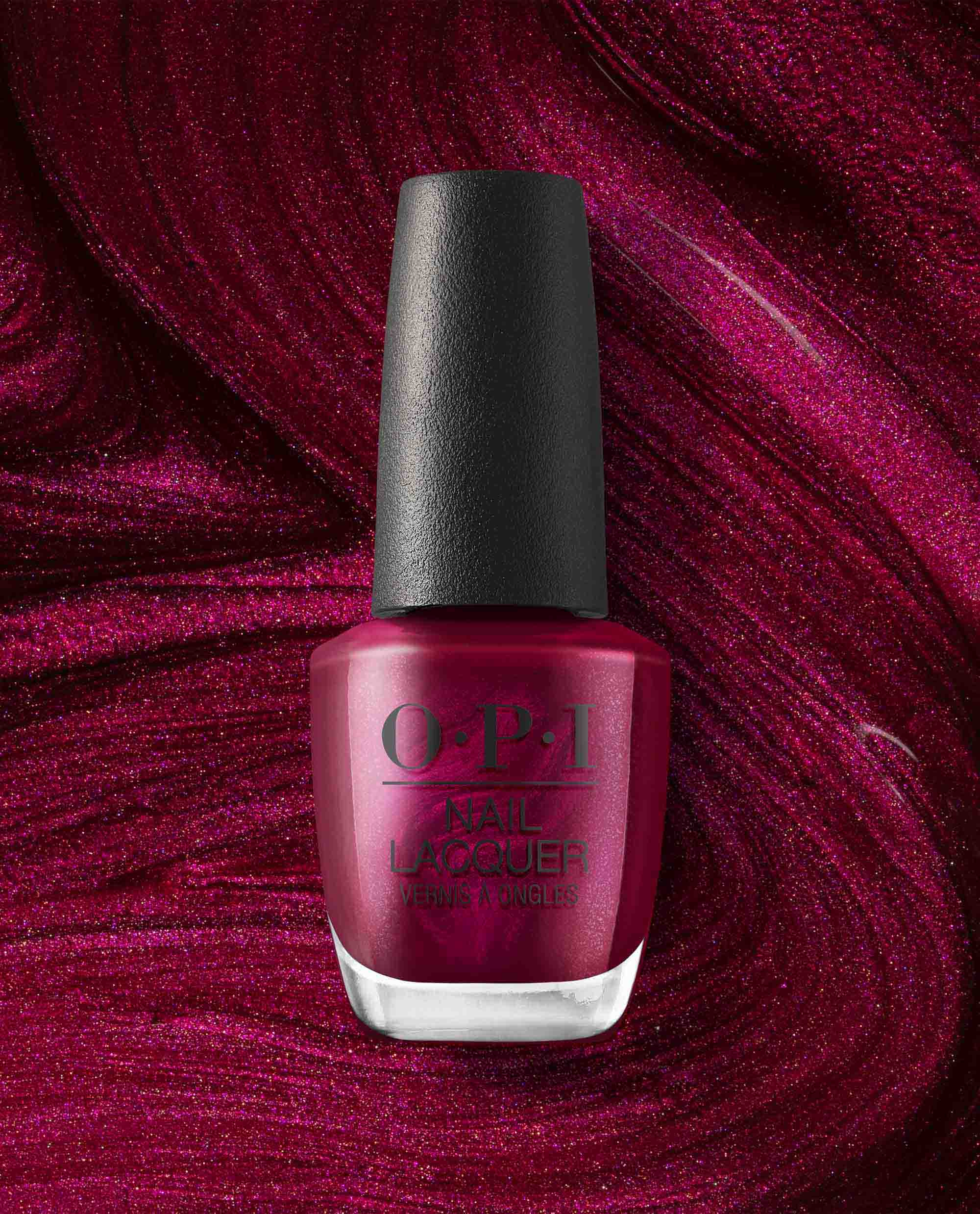 OPI nail polish bottle in the shade Big Sagittarius Energy, a deep shimmery magenta nail lacquer, standing upright against a swirling glittery berry-red background that matches the polish color.