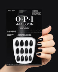 OPI xPRESS/ON Black Onyx press-on nails in glossy black are held beside a manicured hand wearing the extra-short gel-like nails on a dark background, a sleek pick for fall nail colors.