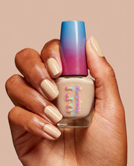 Brown hand holds OPI RapiDry nail polish in Can't Hardly Wait, a trending glossy beige nude shade matching manicured nails, with a blue-to-magenta cap on a warm neutral background.