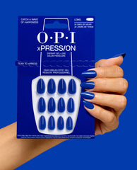OPI xPRESS/ON Catch a Wave of Happiness long cobalt blue press-on nails shown on a hand beside matching retail packaging against a vivid blue background.