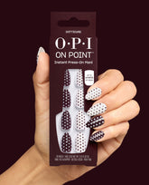 Hand holds OPI On Point Dotticure instant press-on mani in burgundy and white polka dot fall nail colors, shown on matching almond nails against a deep wine background.