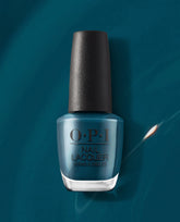 OPI nail polish bottle, Drama at La Scala nail lacquer, standing upright and filled with deep teal blue color against a matching dark teal background, highlighting the glossy finish and black textured cap for a modern manicure look.