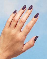 Hand modeling glossy deep plum Eco-Maniac OPI Nature Strong Vegan Nail Lacquer on almond-shaped nails against a blue background, a rich pick for fall nail colors.