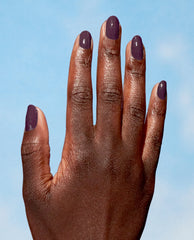 Hand modeling glossy plum-purple Eco-Maniac OPI Nature Strong Vegan Nail Lacquer on short rounded nails against a light blue background, showcasing a rich fall nail color.