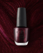 OPI Every Month is Oktoberfest nail lacquer bottle stands against a shimmering burgundy background, showcasing a deep wine-red metallic shade for fall nail colors.