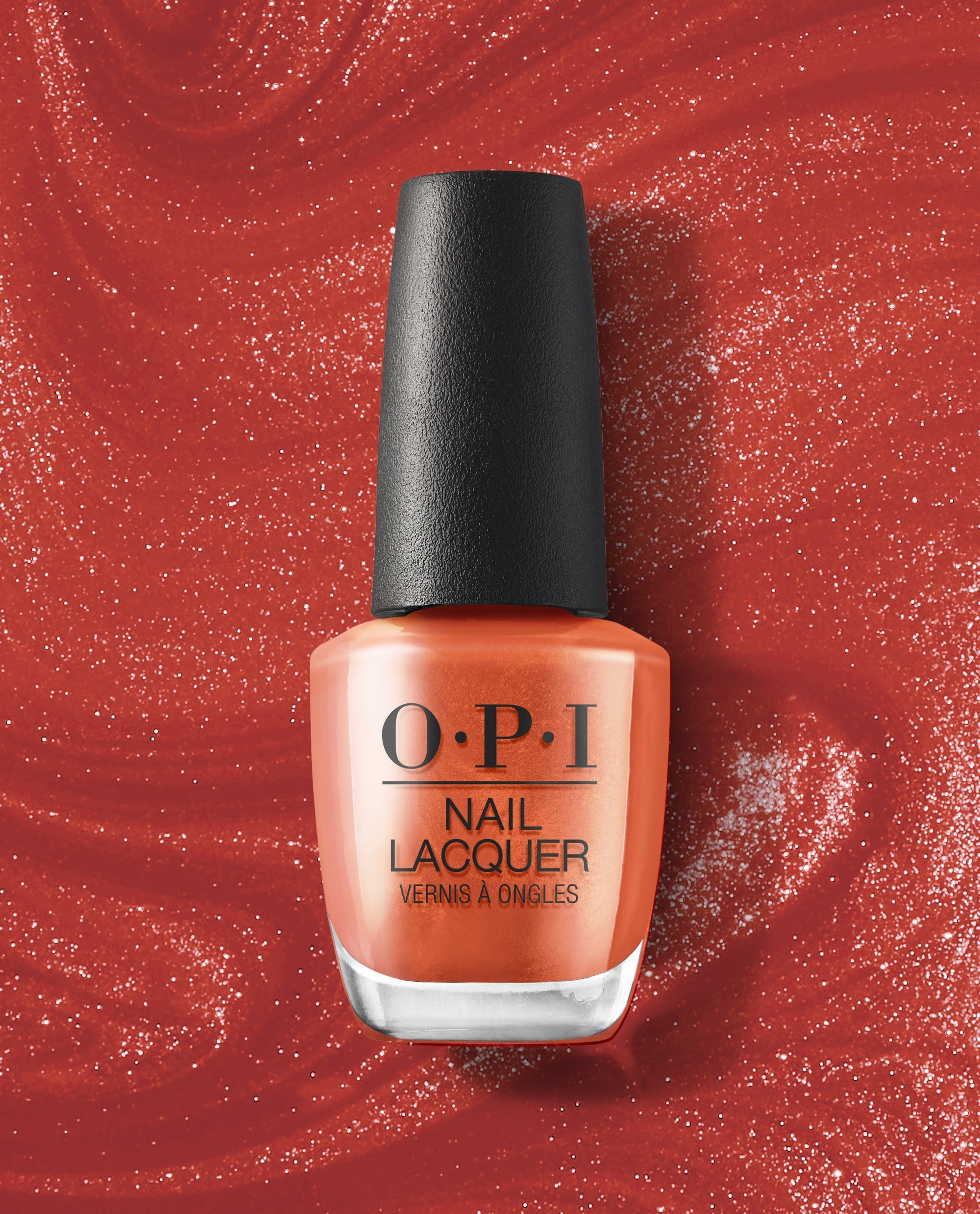 OPI nail polish bottle of Liquid Fire nail lacquer standing upright, showcasing a vibrant metallic orange-red shade with shimmer, set against a swirling glittery red background for a bold, fiery manicure look.