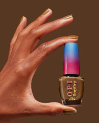 Hand with glossy bronze nails holding OPI RapiDry nail polish in Fast Foodie, a shimmery brown shade for fall nail colors, against a warm chocolate background.