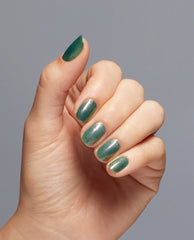 Manicured hand showcases OPI Feelin’ Capricorn-y Dipping Powder, a shimmery green nail polish finish with glossy oval tips catching light, perfect for spring nail colors, against a soft gray background.