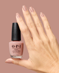 OPI France-y Seeing You Here Nail Lacquer in a glossy muted pink nude coats manicured nails as a hand holds the matching bottle against a mauve background, ideal for fall nail colors.