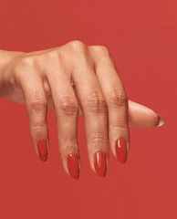 Hand modeling glossy red-orange OPI Infinite Shine nail polish in Full of Glambition, a bold choice for fall nail colors, against a matching red background.