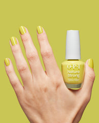 Hand with glossy yellow‑green manicure posed next to an OPI Nature Strong Vegan Nail Lacquer bottle, shade Give Me Some Suga Cane, on a matching lime background—green nail polish perfect for spring nail colors.