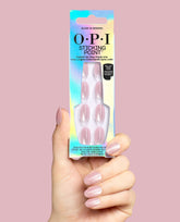 Hand holding OPI Sticking Point Glass in Session no-glue press-on nails in glossy sheer pink, displayed in iridescent packaging against a soft pink background for fall nail colors.