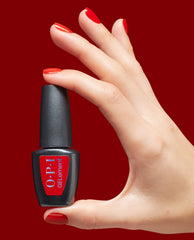 Hand with glossy red manicure holds an OPI GelColor bottle for Glossy Goddess at-home gel nail polish, a bold red shade for fall nail colors, against a deep red background.