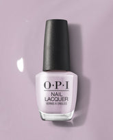 OPI nail polish bottle in the Graffiti Sweetie shade standing upright, showcasing pale lavender nail lacquer with a black cap against a matching soft purple background, highlighting the glossy pastel color for manicures and pedicures.