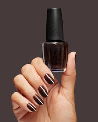 Hand with manicured nails painted in deep shimmery brown holds a Grunge Queen OPI nail polish bottle against a solid dark background, showcasing the rich, glittery nail lacquer color and glossy finish.