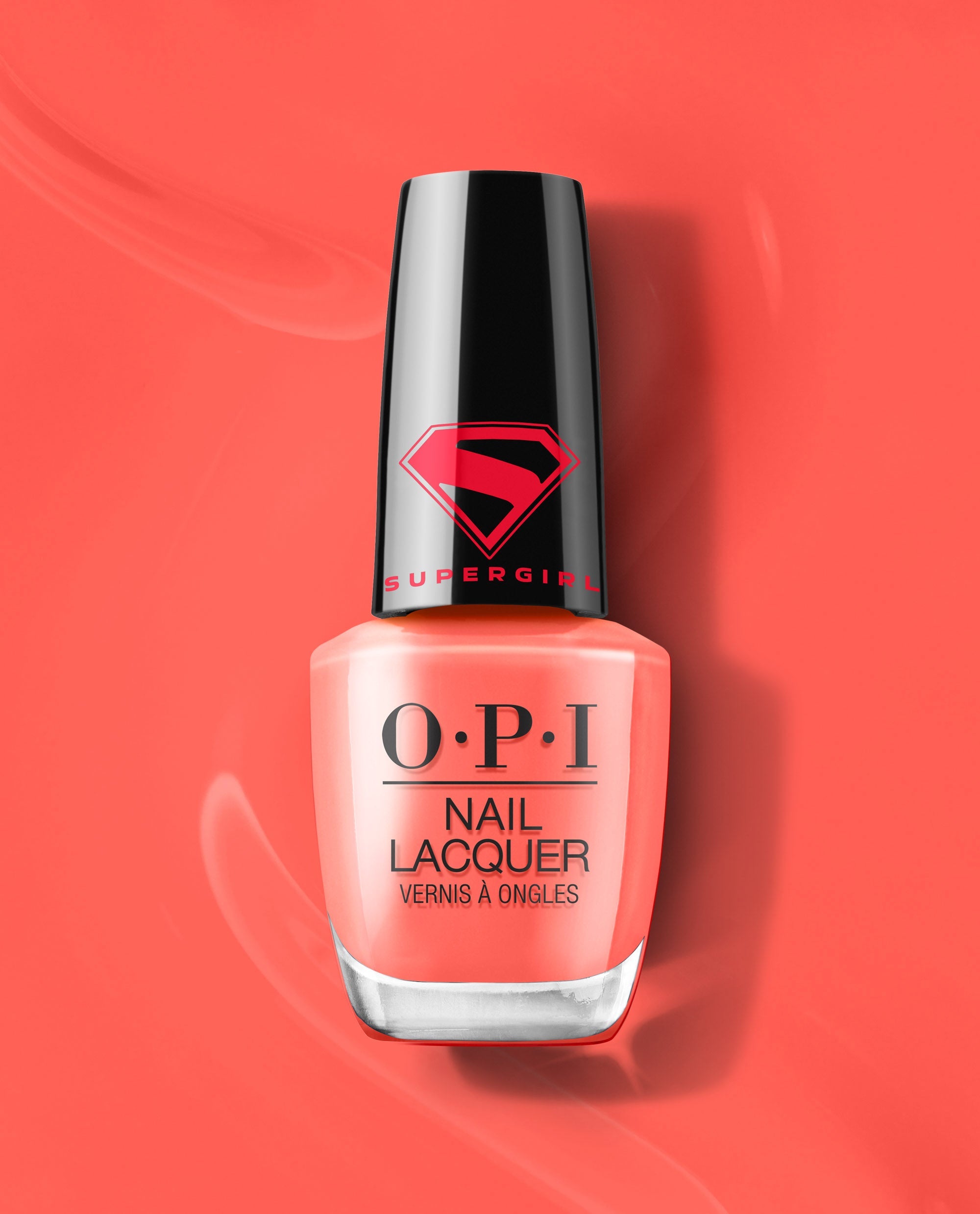 OPI Heat Vision Nail Lacquer bottle stands upright on a glossy coral-red background, showing a peachy coral polish shade and black Supergirl logo cap for a trending manicure look.