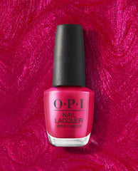 OPI It’s All Greek to Me nail lacquer bottle in vibrant shimmering fuchsia, standing upright with a black cap against a glossy magenta polish swirl, a bold choice for fall nail colors.