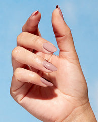 Hand modeling glossy almond nails painted with OPI Kind of a Twig Deal Nature Strong vegan nail lacquer, a soft taupe-mauve shade for fall nail colors, against a blue background.