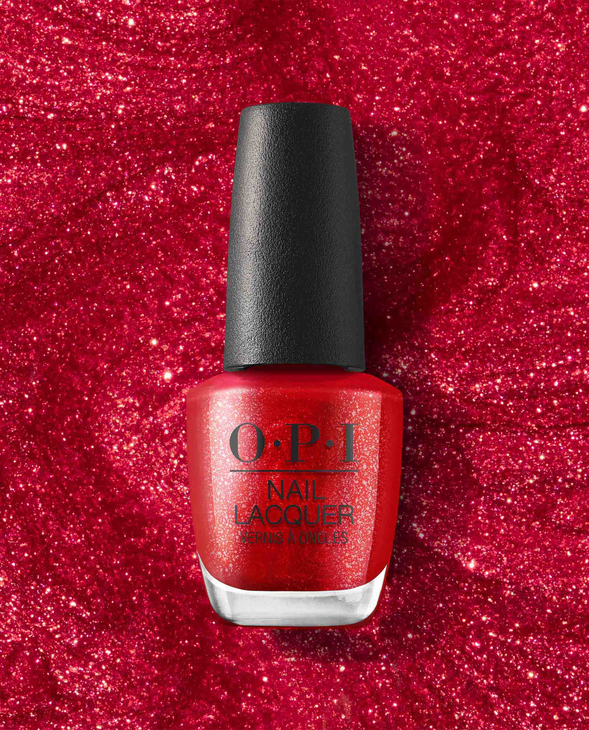 OPI nail polish bottle of Kiss My Aries nail lacquer standing upright against a sparkling red glitter background, showcasing its bright shimmery red shade and black cap for bold, eye-catching manicures.