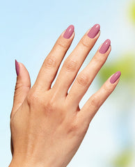 Hand with medium-length oval nails painted in OPI Knowledge is Flower, a dusty rose Nature Strong vegan nail lacquer, held against a bright blue sky, showcasing glossy coverage ideal for an OPI nail polish gift set.