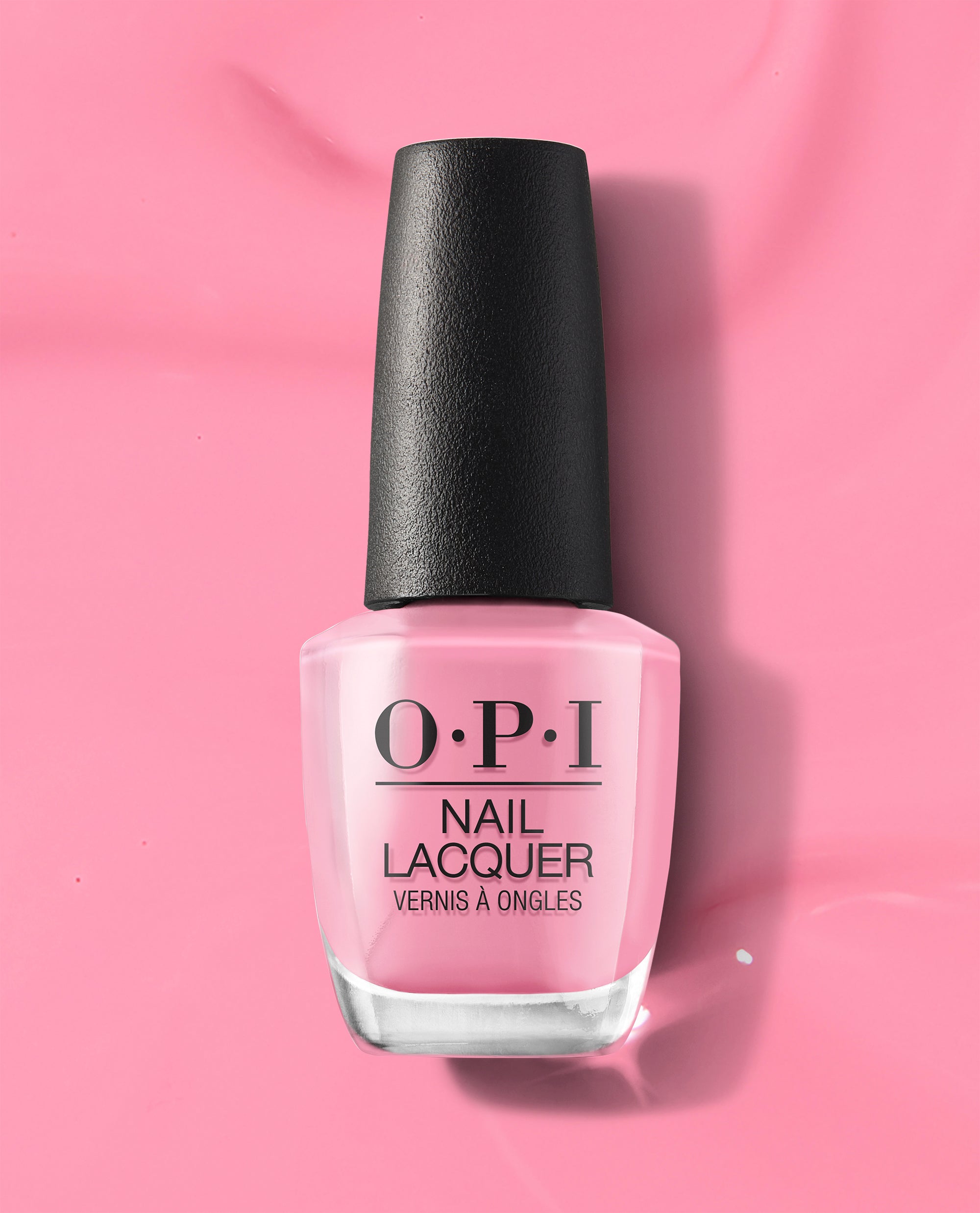 OPI nail polish bottle, Lima Tell You About This Color! nail lacquer, standing upright with a black cap on a glossy solid pink background that matches the soft creamy pink shade inside the clear glass bottle.