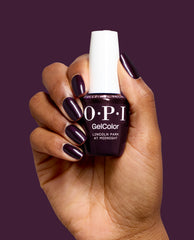 Hand with glossy deep plum nails holds OPI GelColor Lincoln Park at Midnight gel nail polish, a dark purple shade for chic fall nail colors, against a matching plum background.