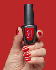 Hand with glossy red shimmer nails holds OPI GelColor Loves Me, Loves Me Hot at-home gel nail polish against a red background, showcasing bold fall nail colors.