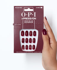 OPI Malaga Wine xPRESS/ON press-on nails in deep burgundy are displayed in classic packaging, held beside a matching manicure for rich fall nail colors.