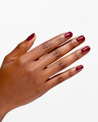 Hand with short rounded nails wearing OPI Infinite Shine Malaga Wine, a glossy deep burgundy shade, shown on a clean white background as a rich option for fall nail colors.