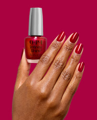 Hand with glossy red wine shimmer nails holds OPI Infinite Shine Malaga Wine Not? gel-like lacquer, a rich burgundy shade for fall nail colors, against a magenta background.