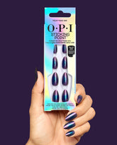 Hand holding OPI Sticking Point Milky Mani Way instant no-glue press-on nails in an iridescent box, with metallic purple and teal almond nails against a deep purple background, ideal for fall nail colors.