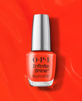 OPI nail polish bottle of Mini Plaid Flirt Infinite Shine in bright orange-red, standing upright with a reflective silver cap on a matching glossy red background, showcasing long-wear gel-like lacquer for manicures.