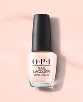 OPI Mod About You Pastel nail lacquer bottle in soft pale pink with a black textured cap, standing on a peach-pink background as a subtle choice for fall nail colors.