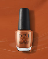 OPI nail polish bottle, shade My Italian is a Little Rusty, standing upright against a matching warm rusty orange background, showing the creamy burnt-orange nail lacquer color in a clear glass bottle with black cap.