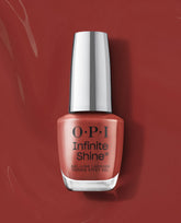 OPI Infinite Shine Nail Prep Rally gel-like lacquer bottle stands upright on a glossy terracotta red background, showcasing a warm coral shade for fall nail colors.