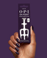 Hand with glossy deep plum press-on nails holds OPI On Point O Suzi Mio Instant Press-On Mani packaging against a purple background, showcasing chic fall nail colors.