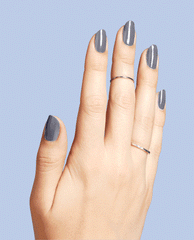 Hand with medium-length nails painted in OPI ❤️ DTLA, a glossy slate-gray OPI nail polish, gently flexing to show shine and coverage against a soft blue background, with thin silver midi rings adding a minimalist, modern look.
