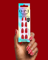 OPI Polka Dot Com Sticking Point press-on nails in glossy red with white polka dots, held on a manicured hand beside iridescent packaging against a red backdrop, a playful pick for fall nail colors.