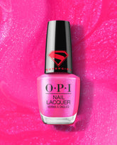 OPI Power up Pink Nail Lacquer bottle in bright shimmery pink, topped with a black Supergirl logo cap, standing on a sparkling hot pink polish background.