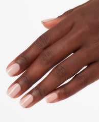 Hand resting against a white background, nails painted with OPI Put it in Neutral nail lacquer in a glossy sheer pink nude shade, showcasing a classic, everyday manicure ideal for an elegant OPI nail polish gift set.