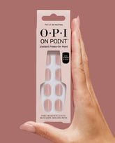Hand with nude almond-shaped nails holding OPI On Point Instant Press-On Mani Put it in Neutral set, showing 24 soft pink artificial nails in a blush box against a matching mauve background, ideal as an OPI nail polish gift set.
