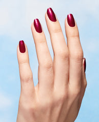 Hand modeling OPI Raisin Your Voice Nature Strong vegan nail lacquer, a shimmery deep berry red manicure shade for fall nail colors, against a soft blue background.