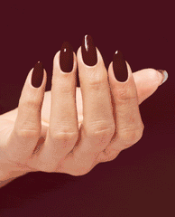 Hand displays glossy almond nails painted OPI Infinite Shine Raisin' The Bar, a deep raisin-burgundy shade for fall nail colors, against a matching wine-red background.